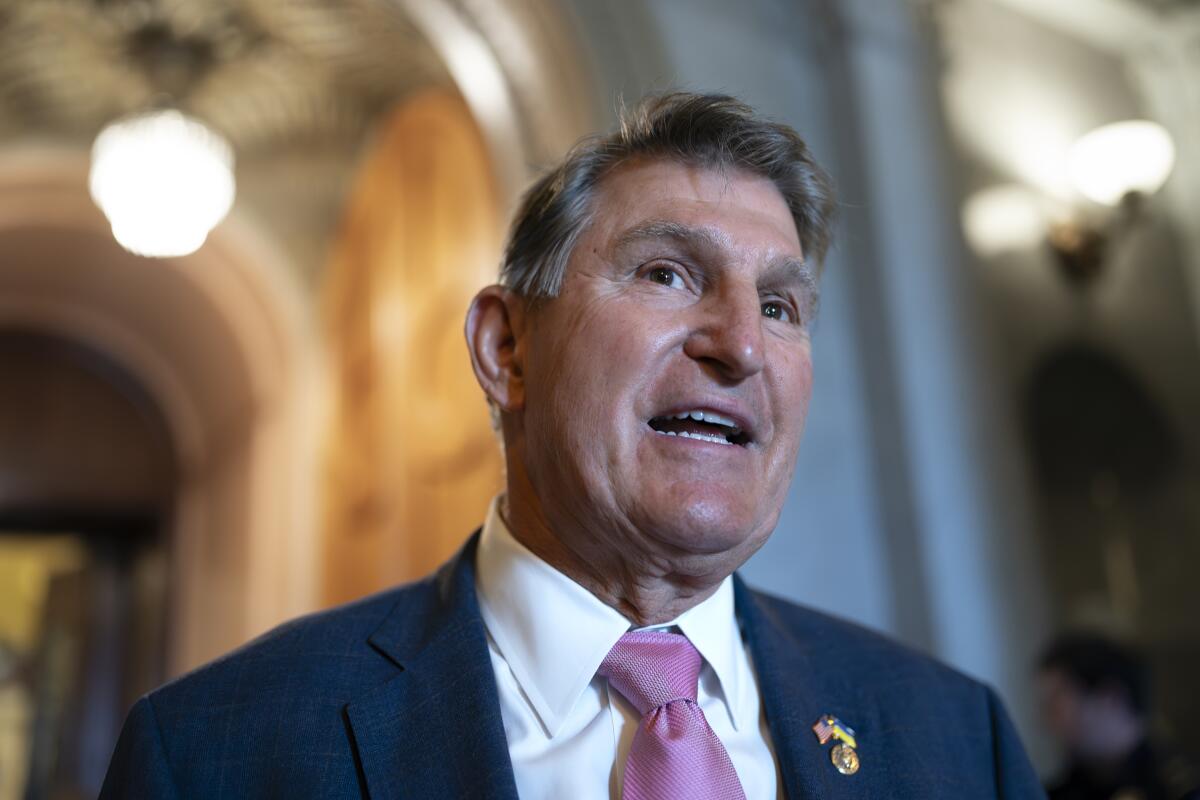 Sen. Joe Manchin III pictured from the shoulders up in a blue suit jacket and pink tie, talking in an ornate hallway.
