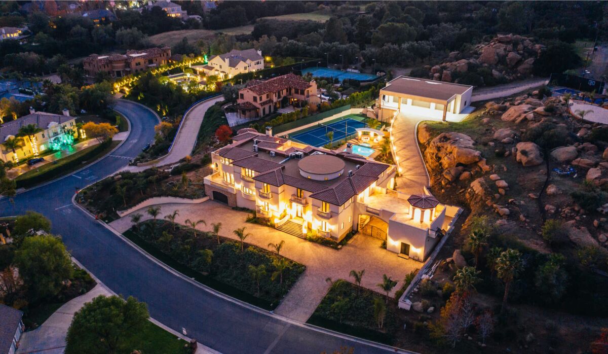 Aerial nighttime view of a mansion lighted up, with swimming pool.