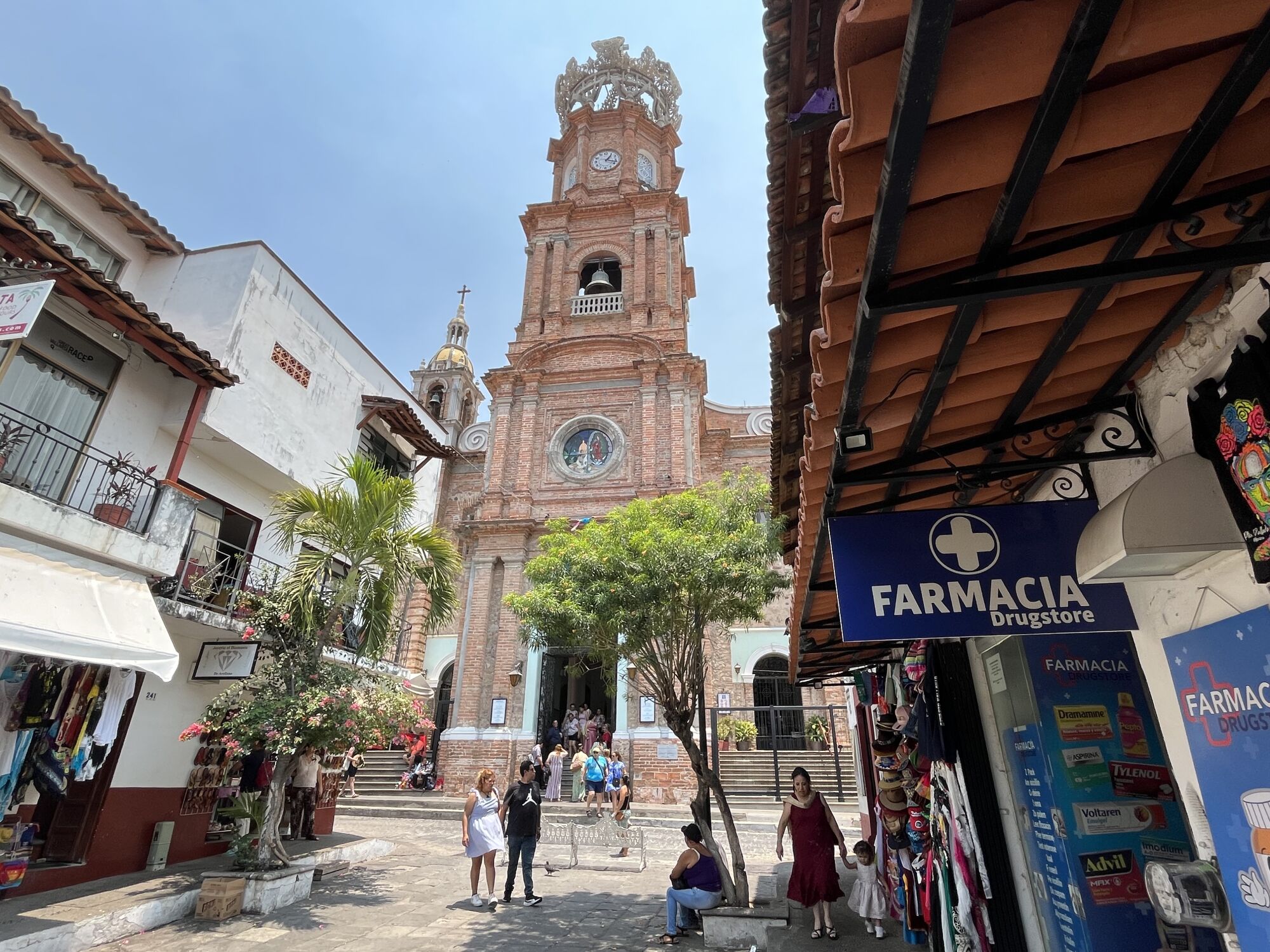 A sign for a pharmacy is seen along a street leading to an ornate church tower.