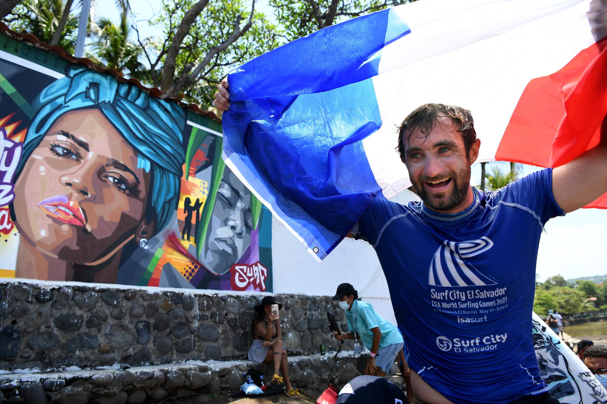 French surfer Joan Duru celebrates as he is carried past a mural of the late fellow surfer Katherine Díaz