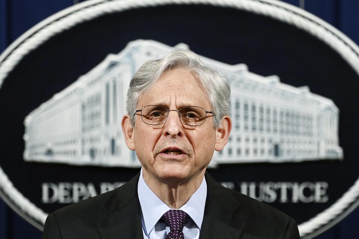 A gray-haired man with glasses speaking in front of a Department of Justice backdrop 