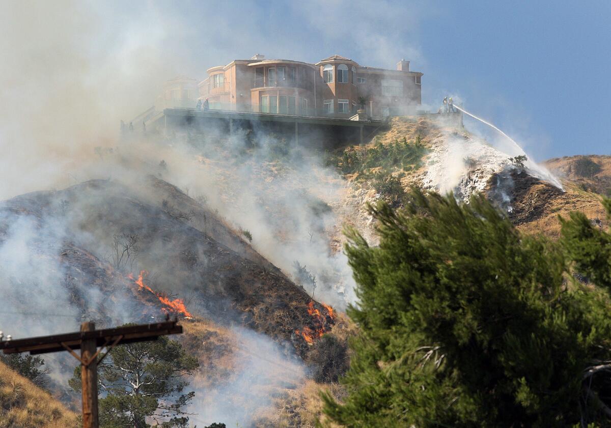 A home on the top of the hill on Irving Drive is protected from a brush fire with a foam sprayed onto the hillside below it in the foothills above Hamline Place in Burbank. (Tim Berger / Burbank Leader)