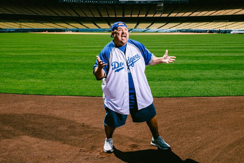 A man poses in Dodgers gear on a sunny day on the field at Dodgers Stadium