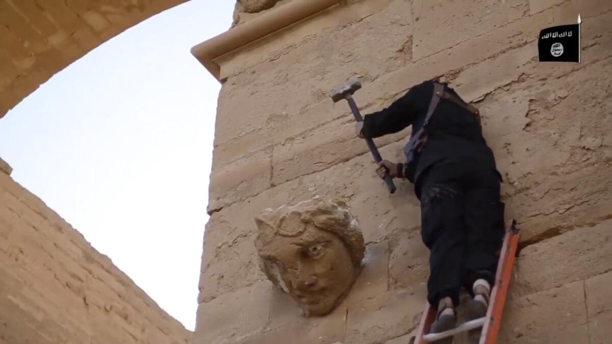 A militant hammers away at a face on a wall in Hatra, a fortified Iraqi city recognized as a UNESCO world heritage site.