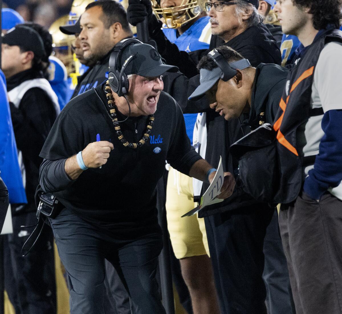 UCLA coach Chip Kelly talks with defensive line coach Ikaika Malloe on the sideline during a 2023 game against Cal 