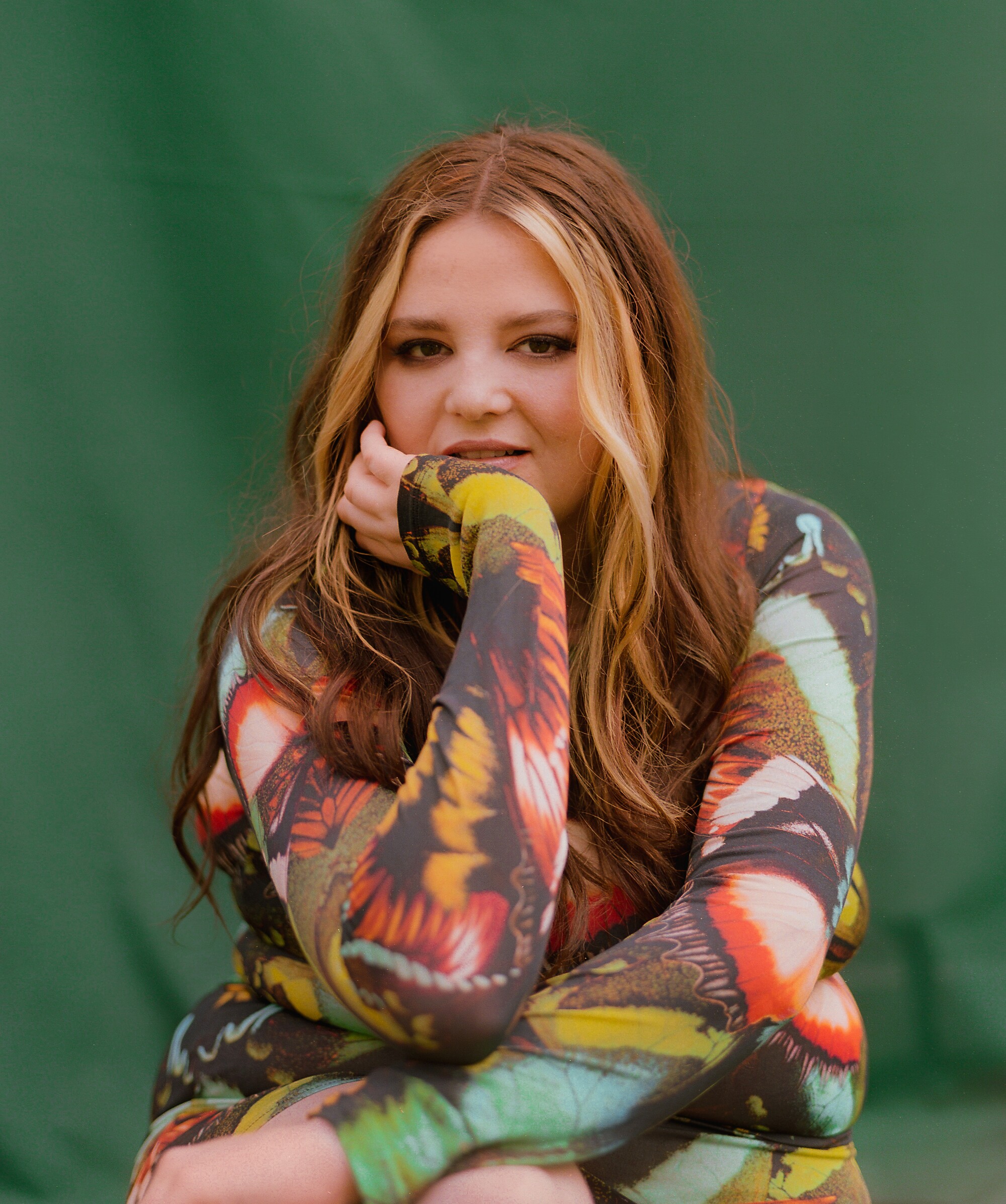 A woman poses for a portrait against a green fabric background.