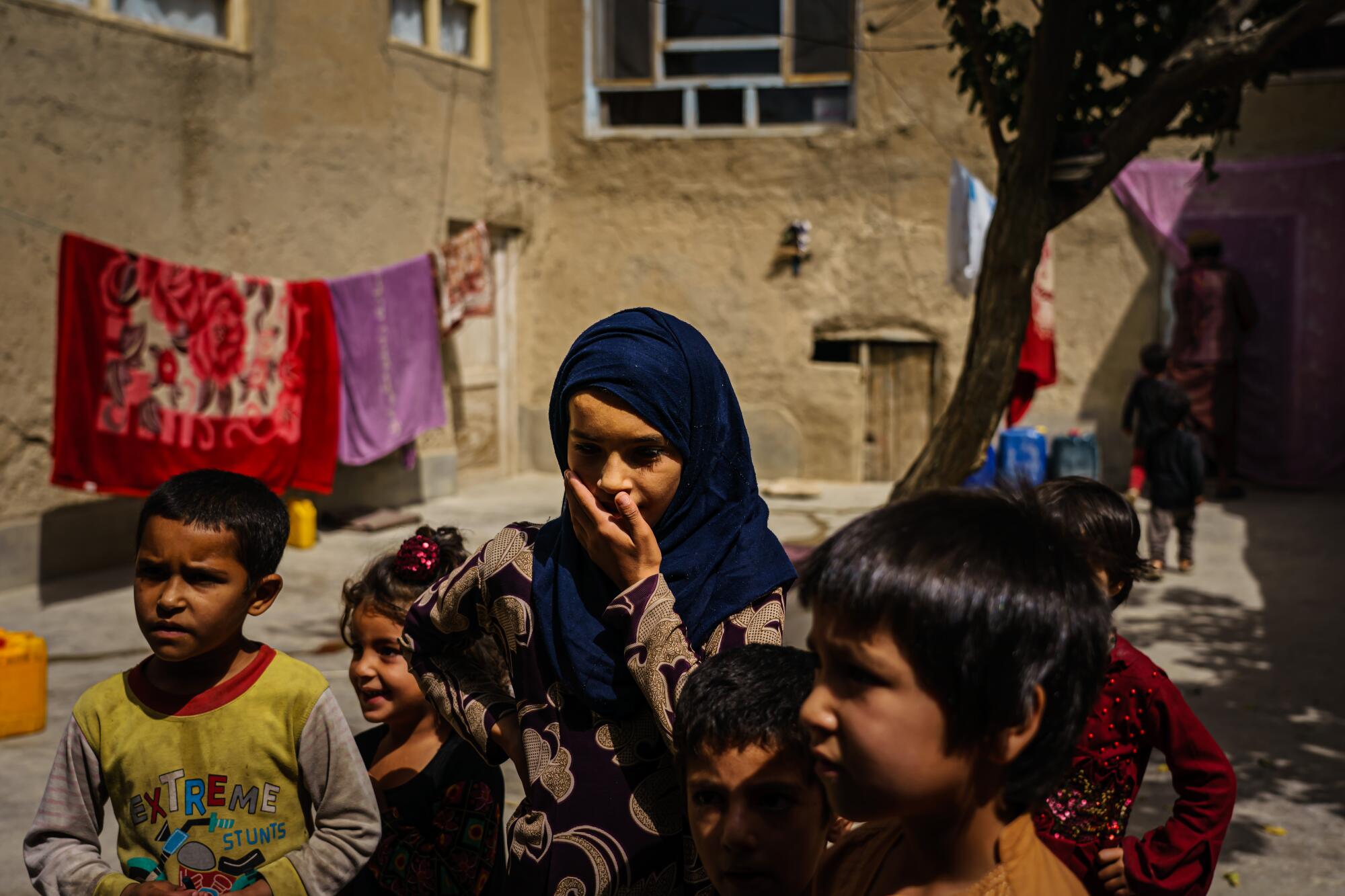 An Afghan girl is flanked by other children in a courtyard.