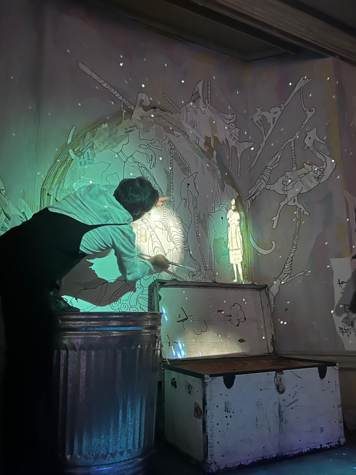 An actor appears drawing on a wall with a wand, where an animated figure appears. 