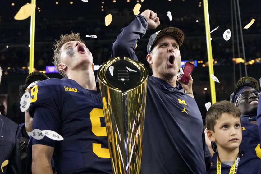 Michigan head coach Jim Harbaugh and quarterback J.J. McCarthy celebrate with the College Football Playoff trophy 
