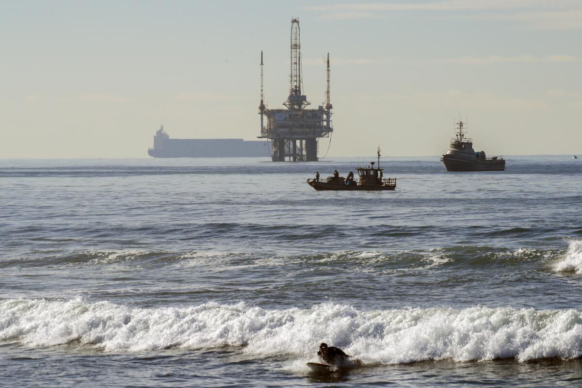 Boats survey behind the surf with oil rigs in the background.
