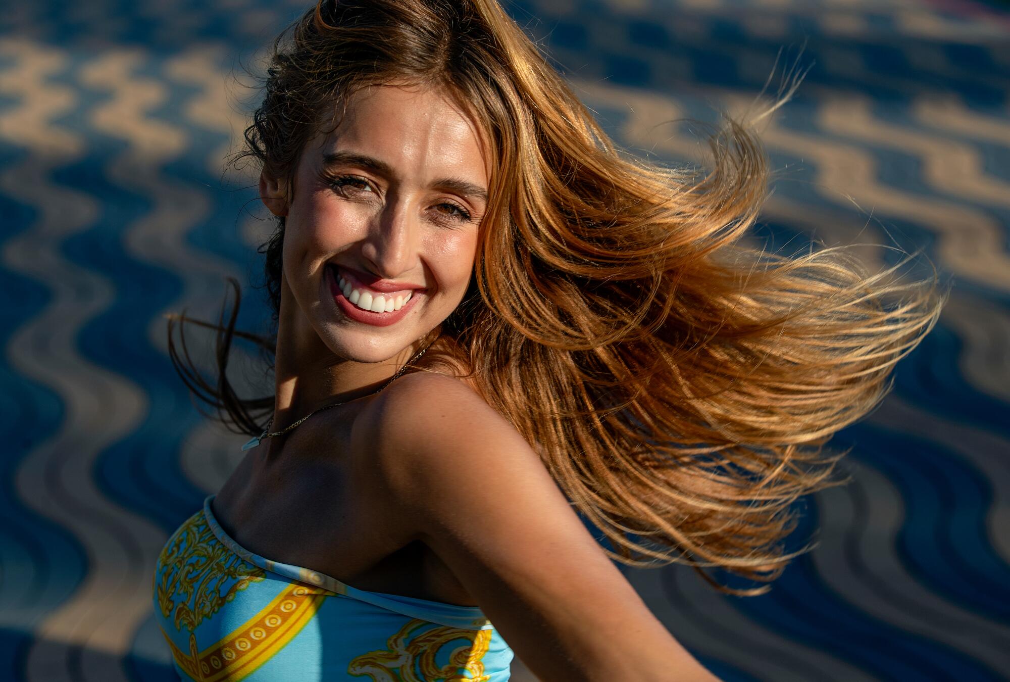 A smiling woman, her long golden hair flying out behind her, turns to look over her shoulder