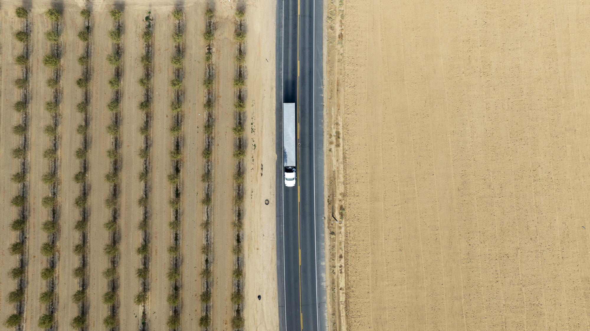 In an aerial view, a tractor-trailer is on a road in a rural area.