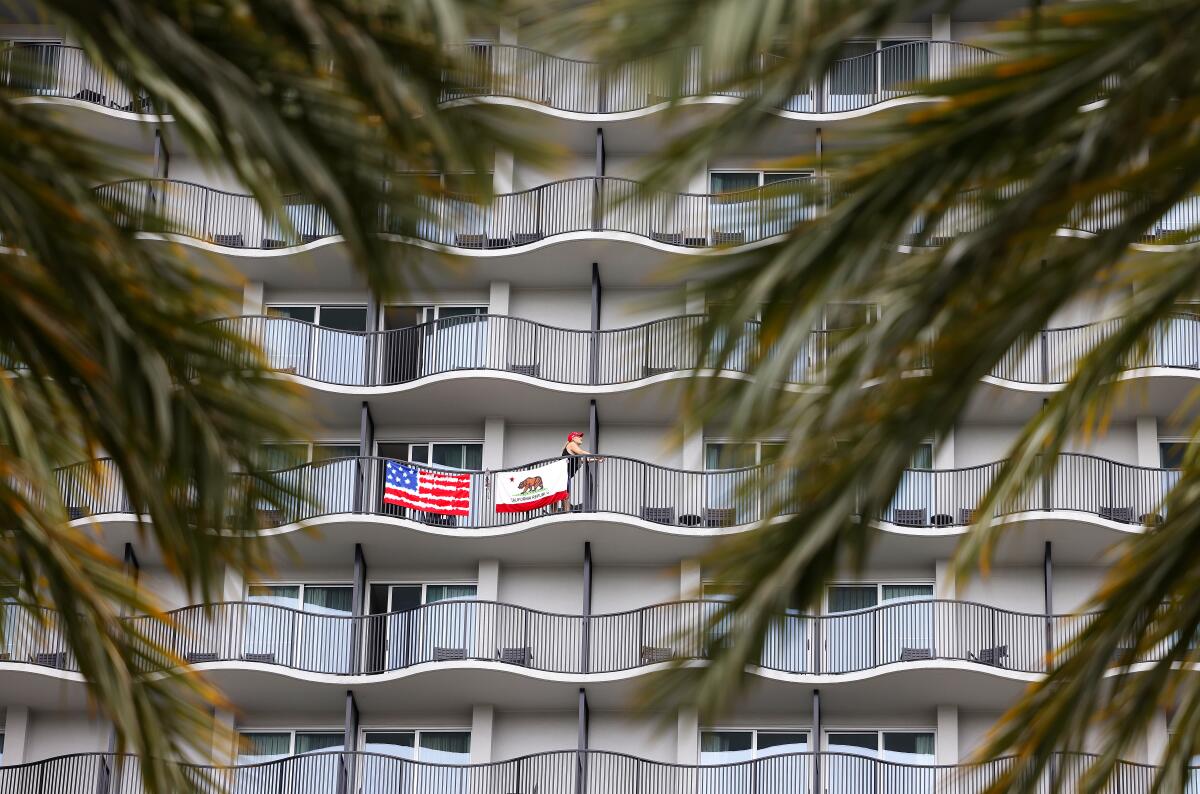 Green branches frame several stories of a hotel with curving balconies, two of them draped with American and California flags