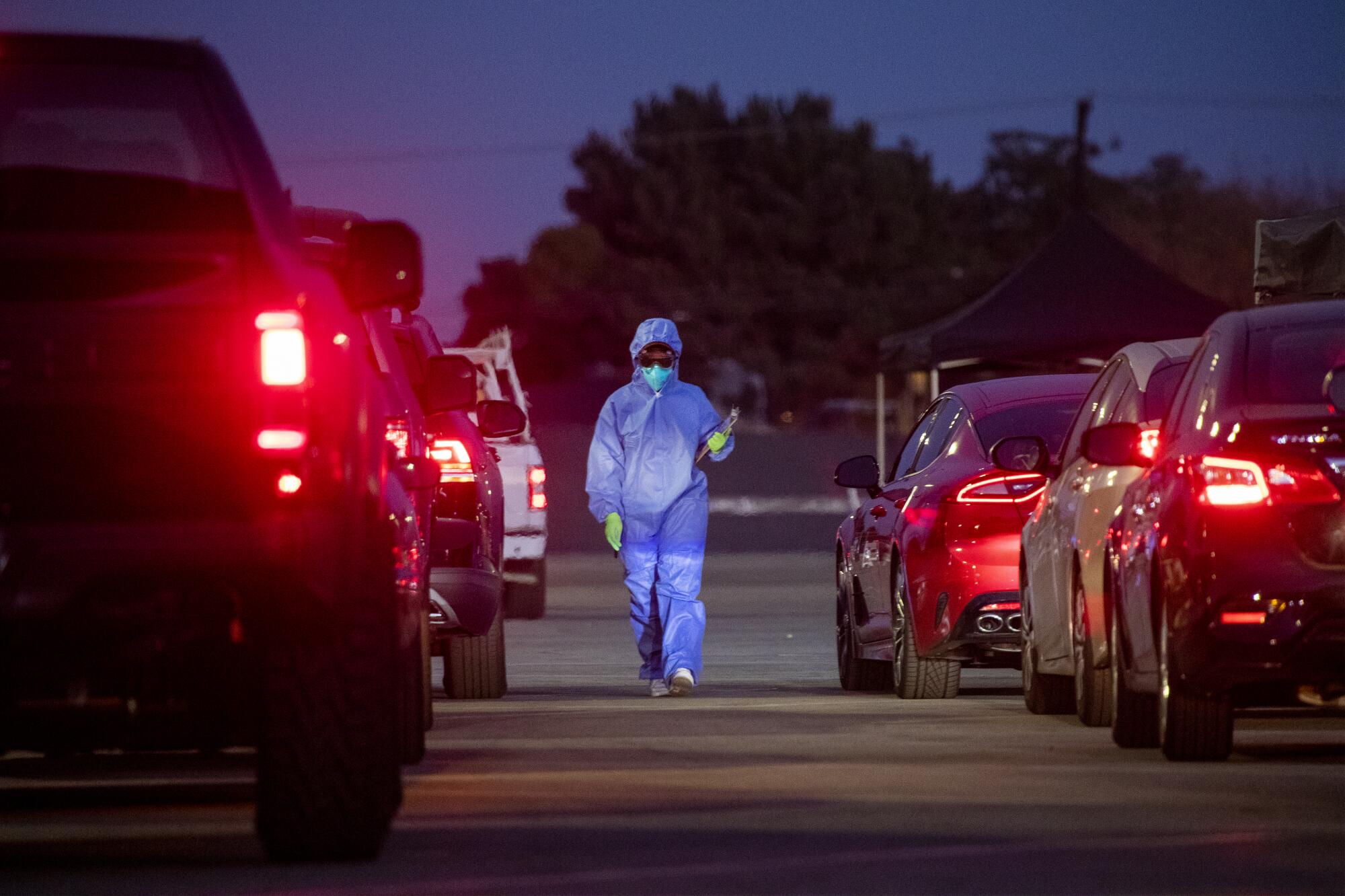 A Health care worker walks between long lines of vehicles at Long Beach City College