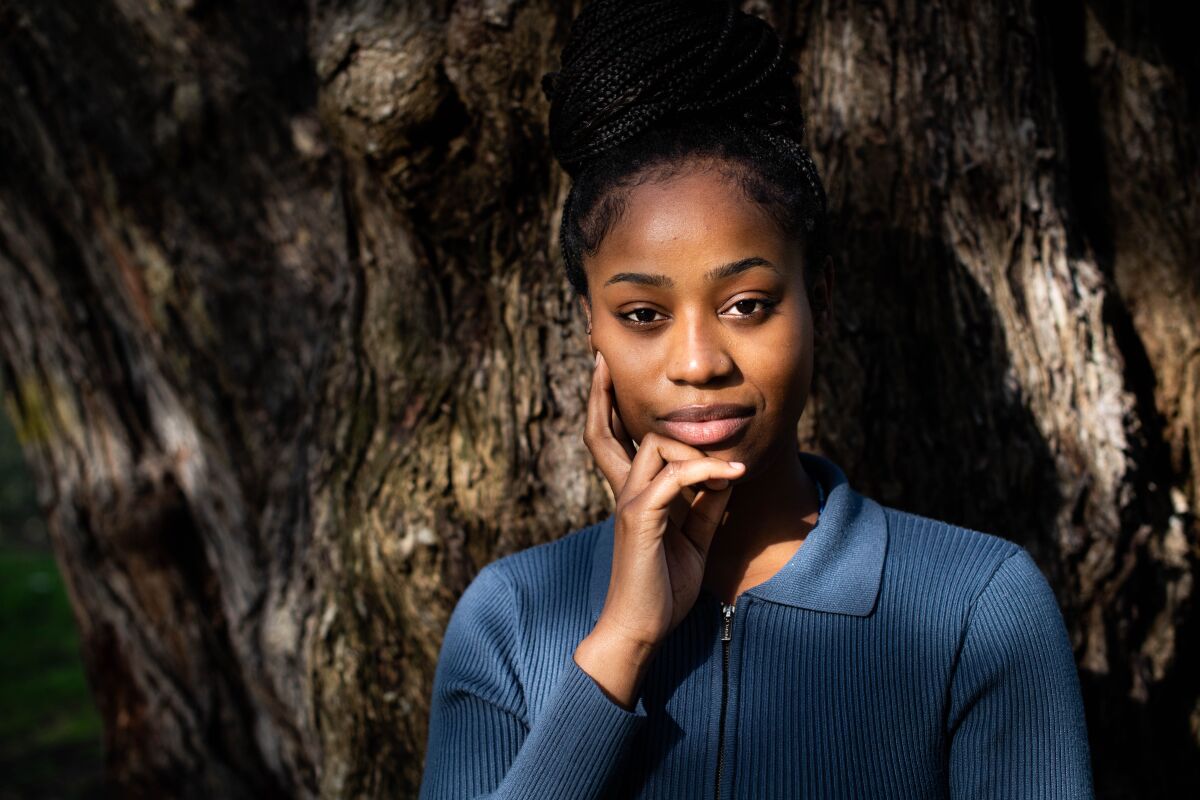 Kefa Ubwenge, 18, standing in front of a tree, her hand holding her face 