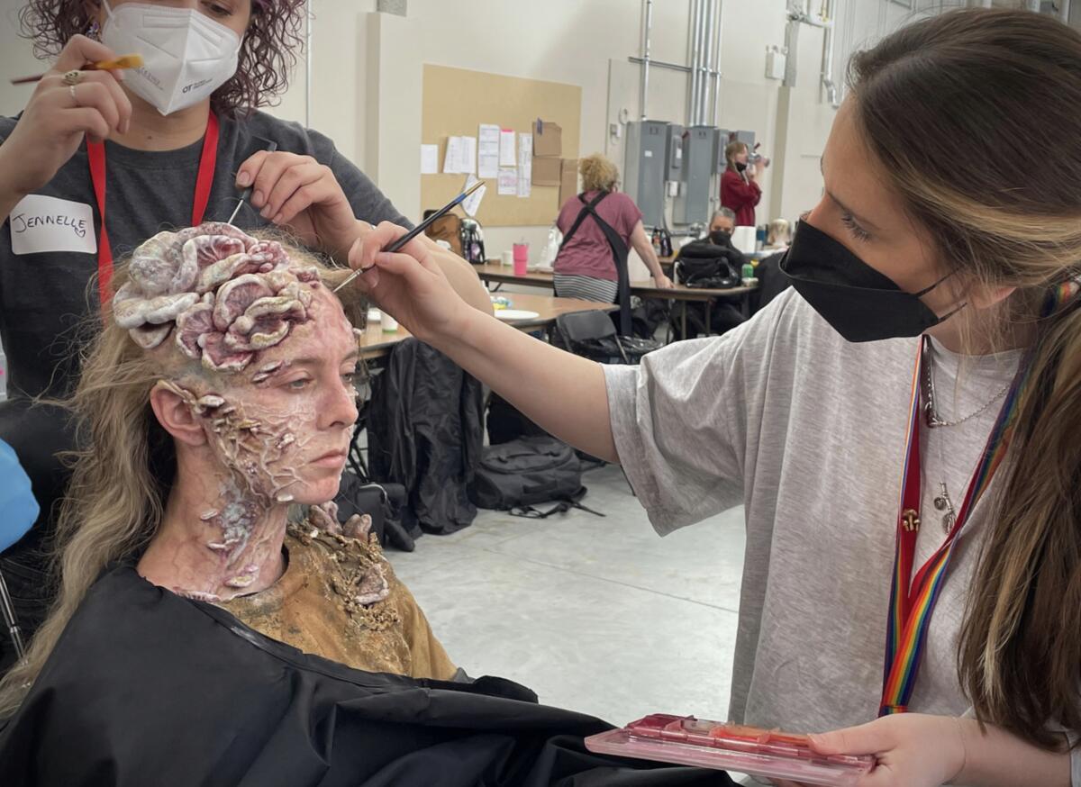 Two women apply touchups to a woman being made up as an infected creature.