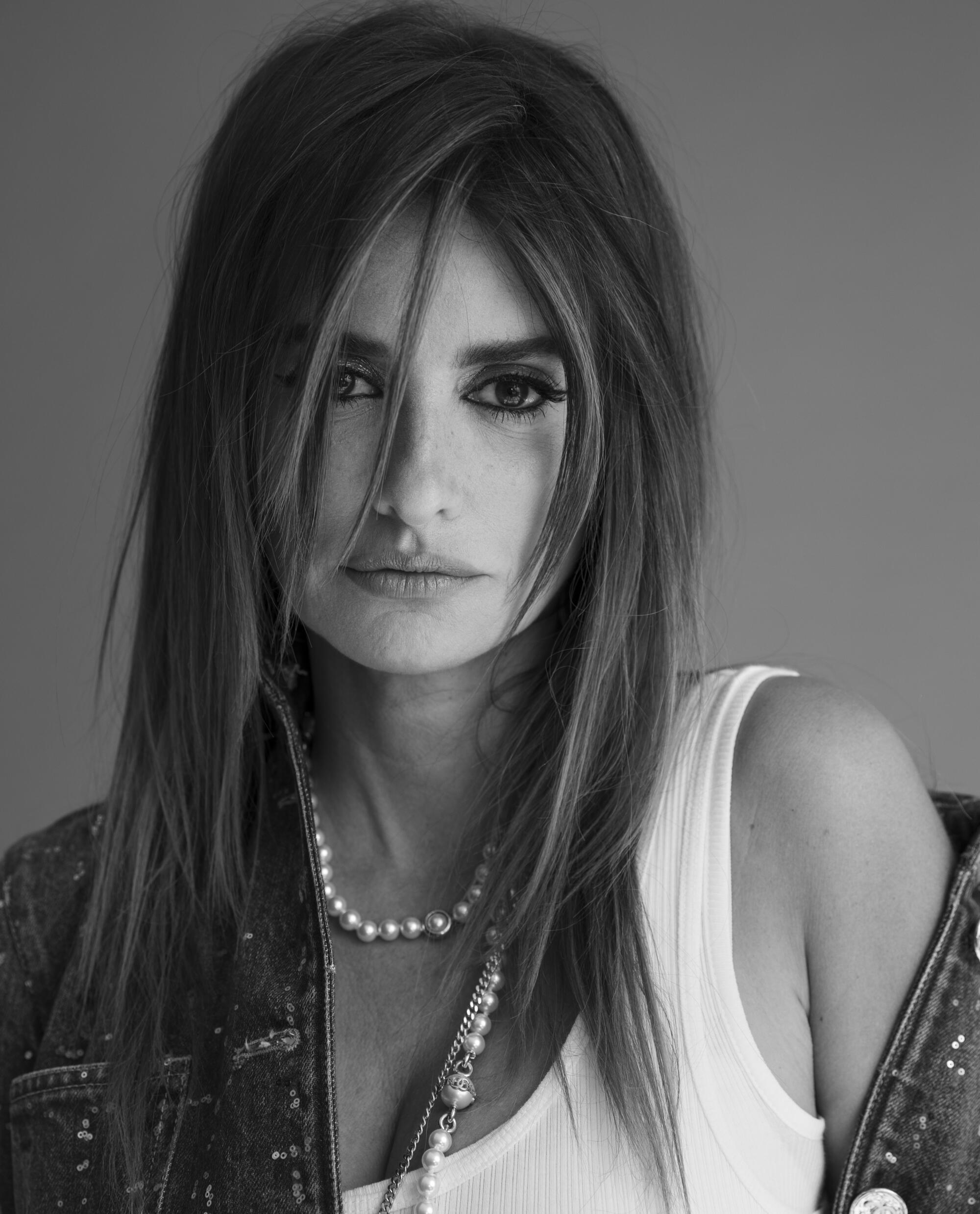 Penélope Cruz wears a pearl necklace, white tank and a denim jacket, with one shoulder uncovered.