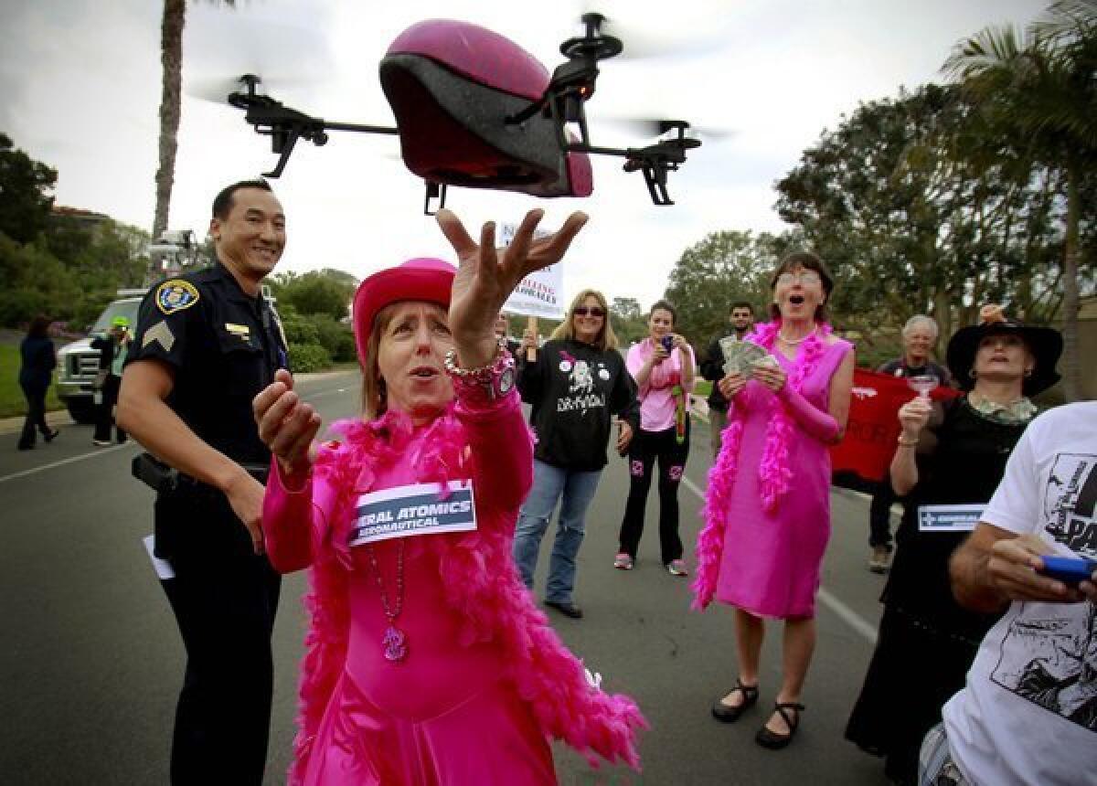 San Diego Police Sgt. Dan Sayasane looks on in La Jolla as a small drone lands in the hand of anti-drone protester Medea Benjamin.