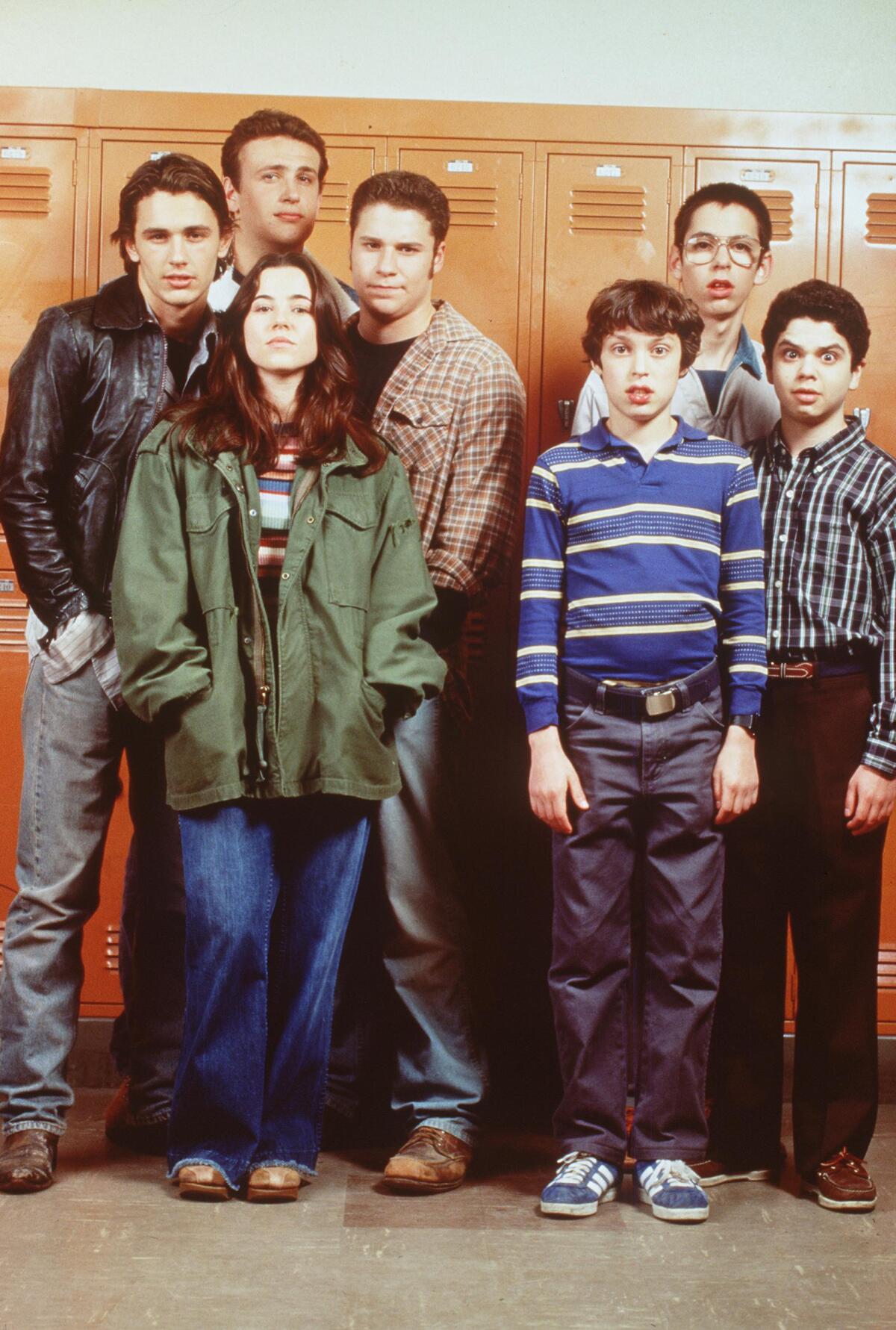 The cast of "Freaks And Geeks" standing against orange lockers.