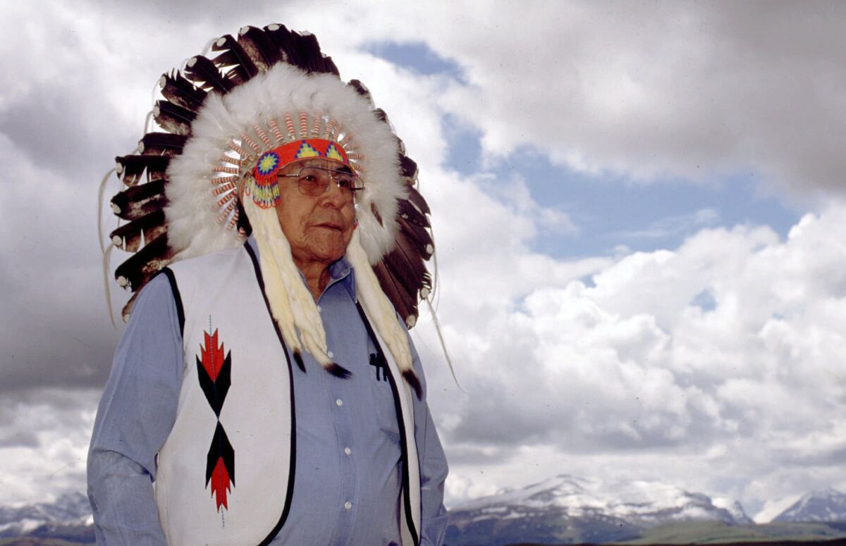 FILE - Earl Old Person, chief of the Blackfeet Nation in Browning, Mt., wears a ceremonial headdress at his home overlooking the Rocky Mountains near Glacier National Park, Mont., on June 9, 1998. Old Person had been on the tribal council on and off since the 1950s and was named chief in 1978. Old Person died Wednesday, Oct. 13, 2021, in Browning, after a long battle with cancer, the tribe said. He was 92. (Stuart S. White/The Great Falls Tribune via AP, File)