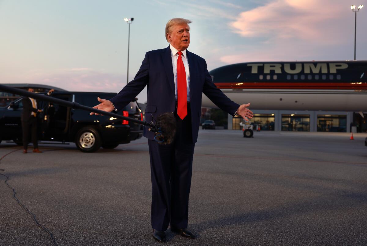 Former President Trump standing in front of a plane and car. 