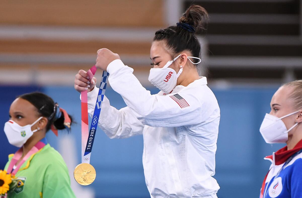 U.S. gymnast Suni Lee picks up her gold medal while standing on the podium after the women's all-around final.