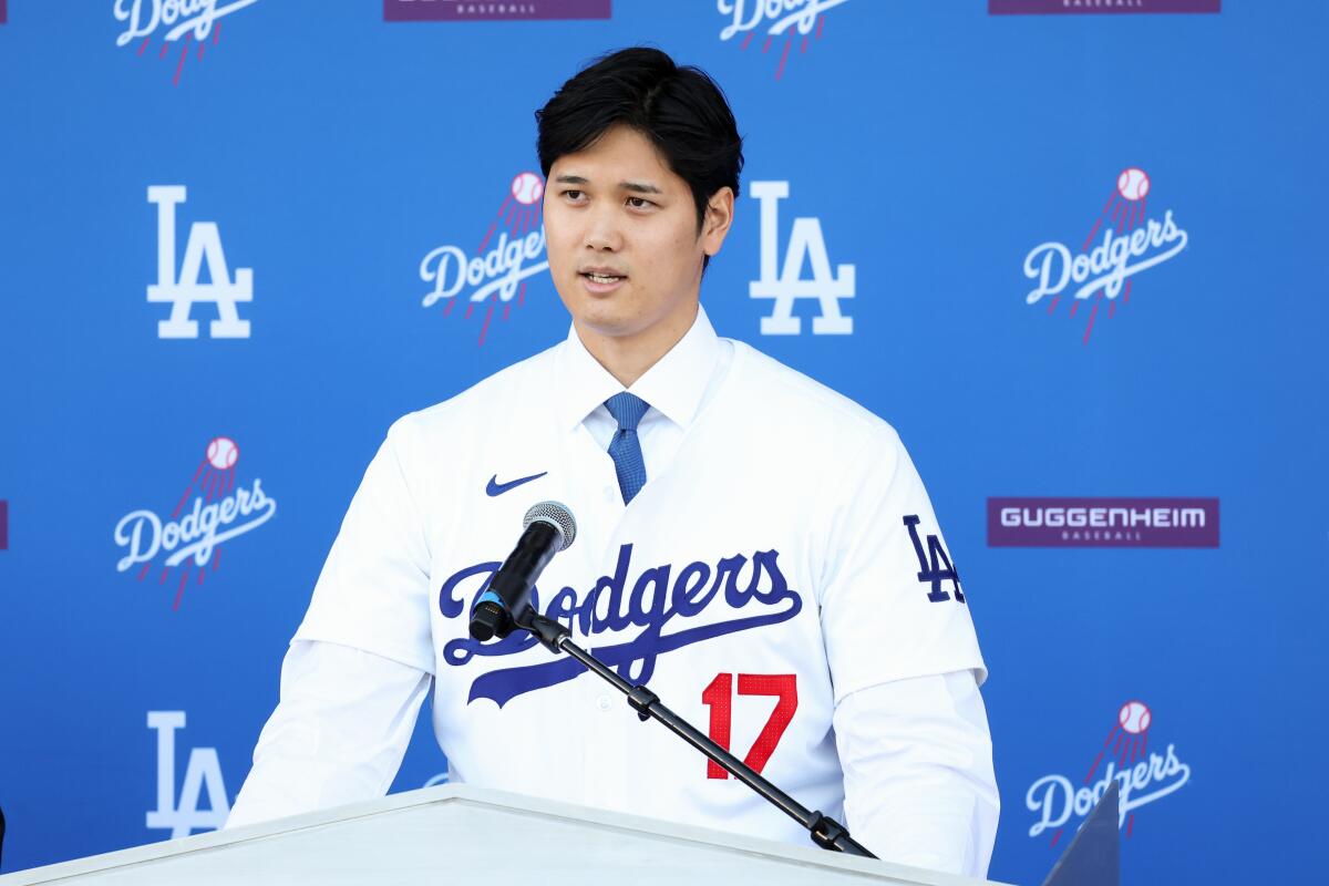 Shohei Ohtani wears a Dodgers uniform and speaks at a microphone