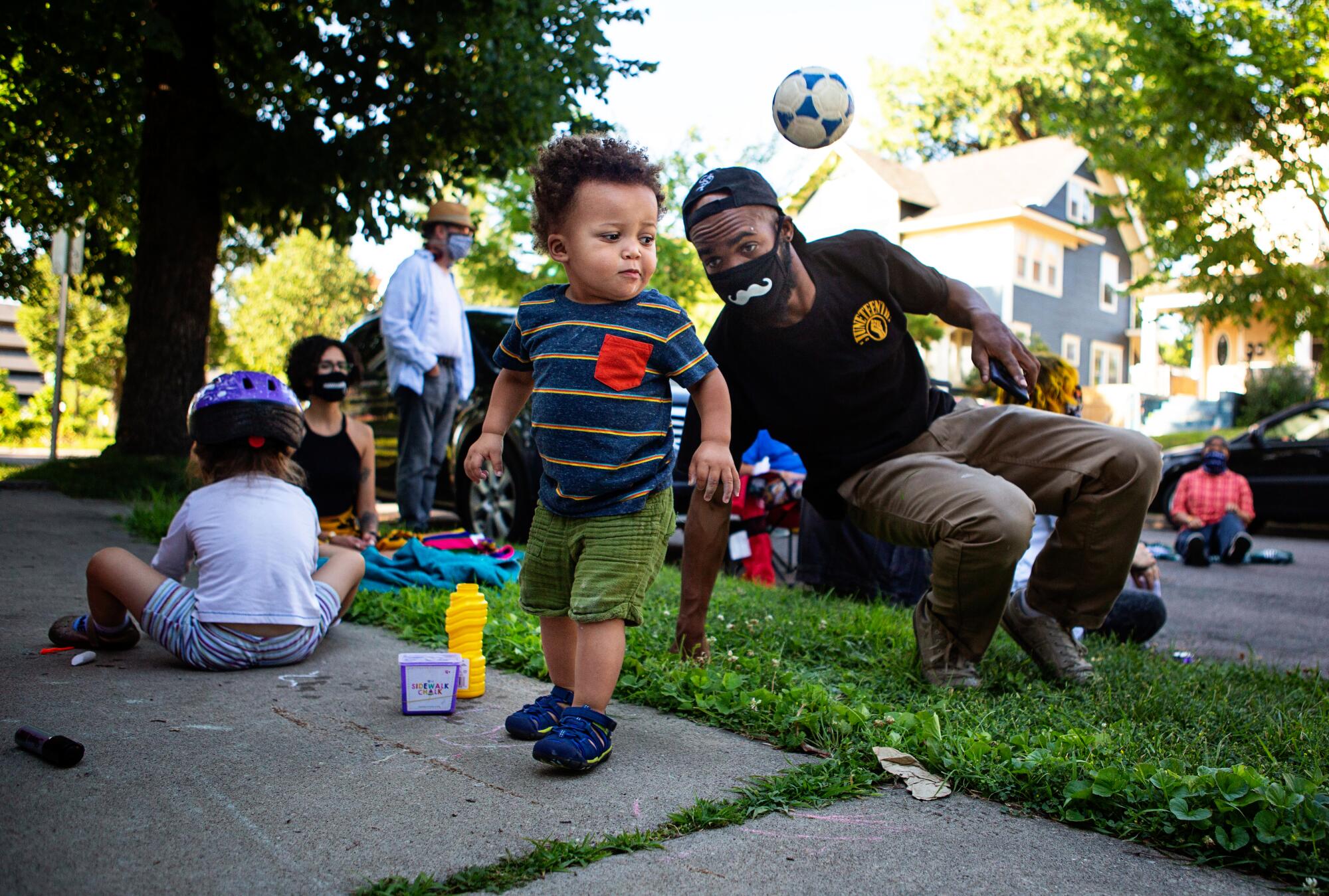 A toddler plays with a ball as his father watches at a community gathering led by Alicia Smith in Minneapolis