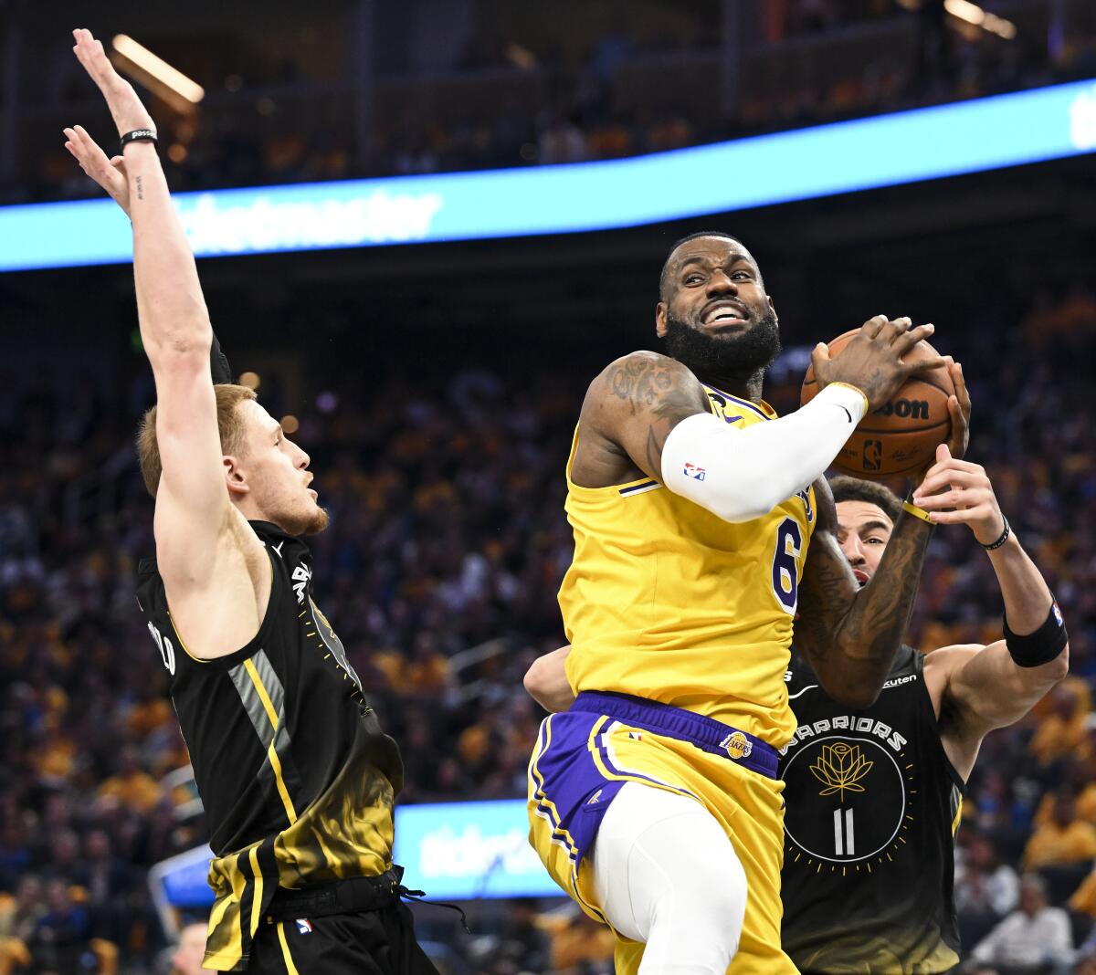 Lakers forward LeBron James, center, elevates for a layup against Warriors guards Donte DiVincenzo, left, and Klay Thompson.