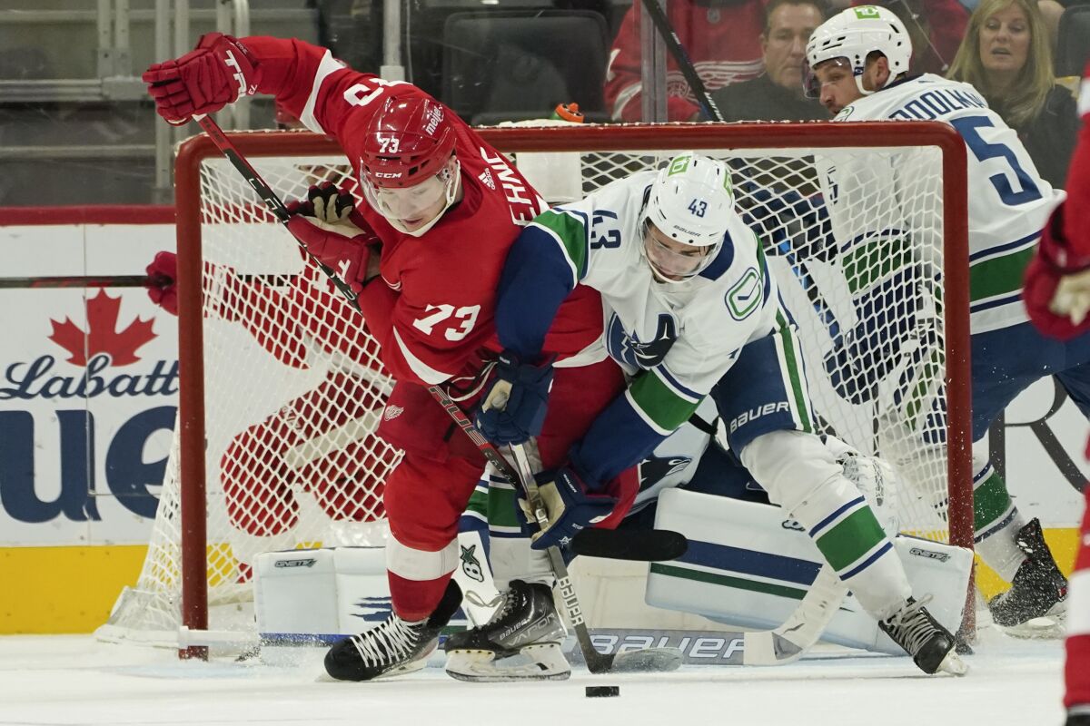 Detroit Red Wings left wing Adam Erne (73) and Vancouver Canucks defenseman Quinn Hughes (43) battle for the puck in the second period of an NHL hockey game Saturday, Oct. 16, 2021, in Detroit. (AP Photo/Paul Sancya)