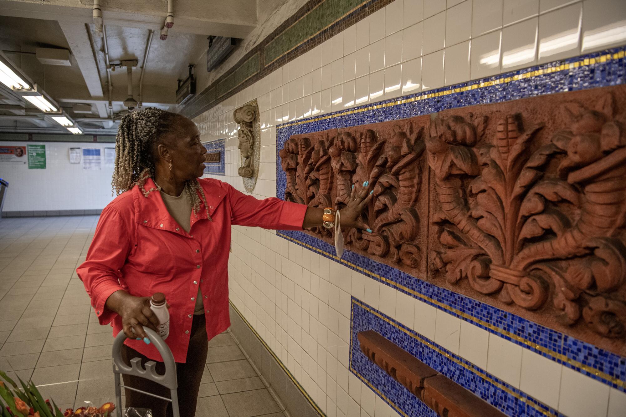 A woman reaching out to touch a large terra cotta relief surrounded by small blue tiles on a subway wall