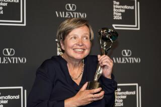 A woman with short light-brown hair smiling and holding a trophy with both hands while clad in a black blouse