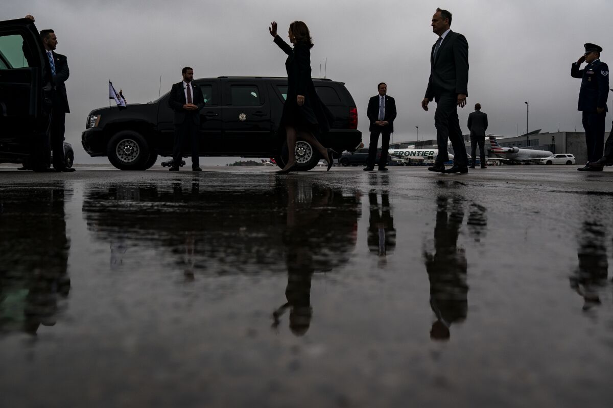 A woman waves and a man walks behind her across a wet tarmac at an airport.