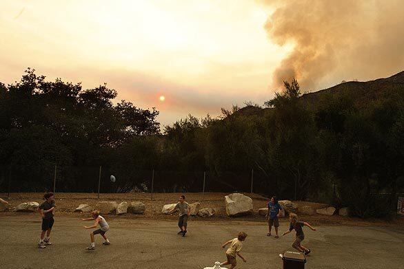 Kids play football after being allowed to return to their homes on Goss Canyon Avenue with the Station fire still burning beyond the charred hills in La Crescenta on Tuesday. "Yesterday it was a battle zone. Now it's a football field again," said resident John Kornarens, who has lived on the street for two years.