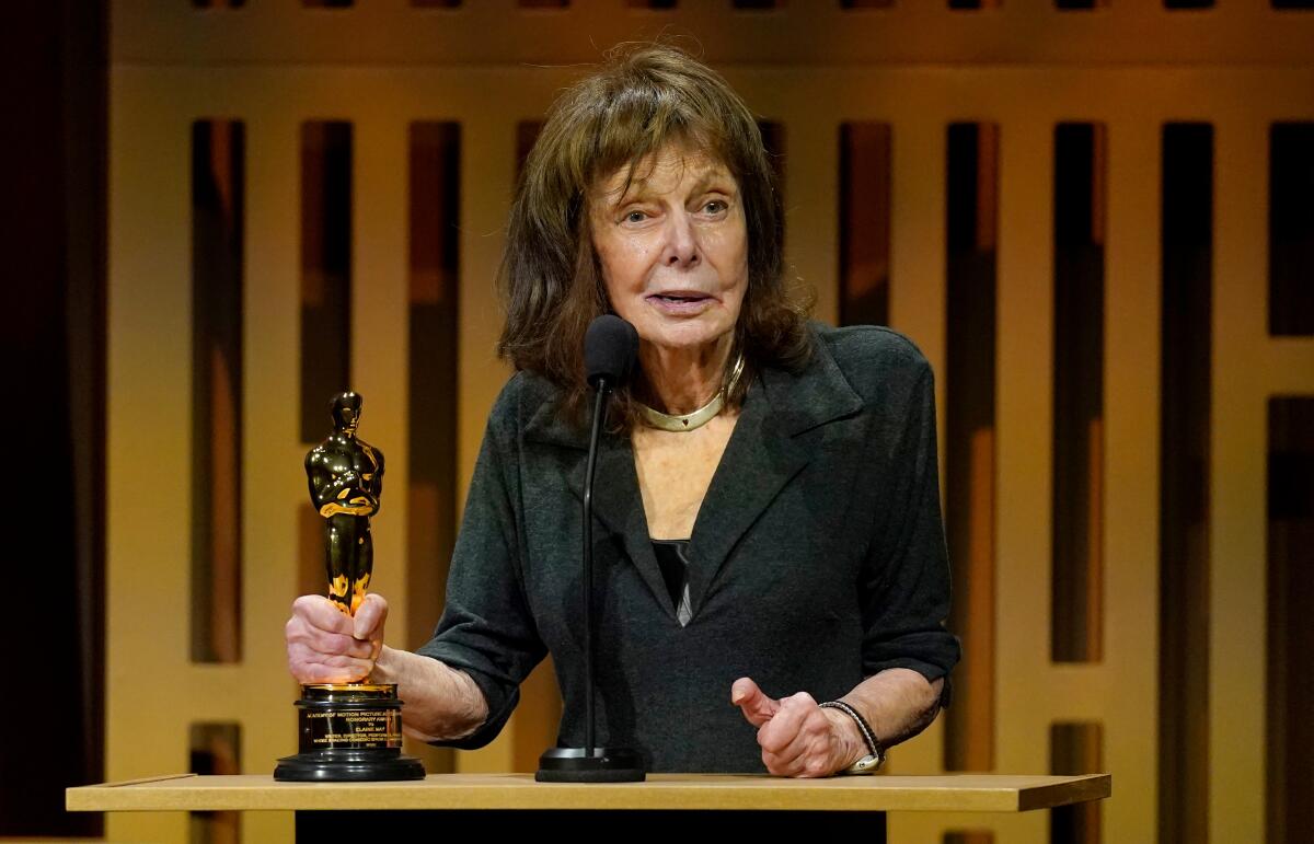 Elaine May talks into a mic while holding an Oscar. 
