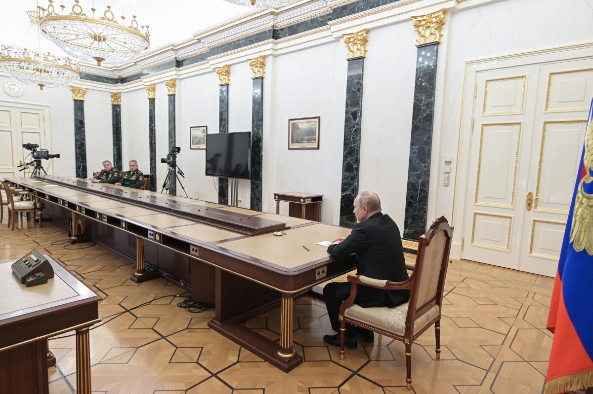 Vladimir Putin sits alone at the end of a long table, talking to military leaders from a distance