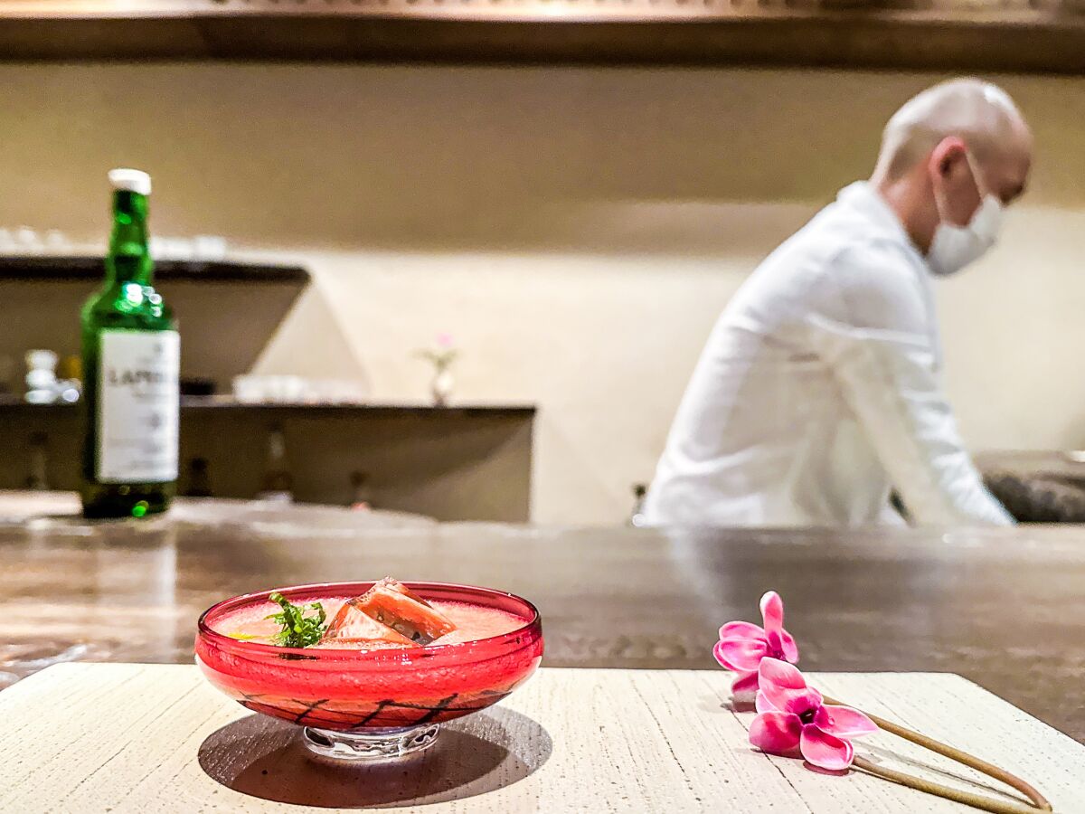 A cocktail in a shallow glass sits on a counter as a chef works in the background