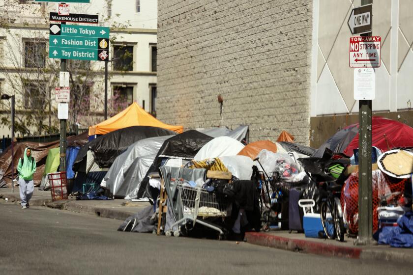 LOS ANGELES, CA - MARCH 26, 2020 - A man walks along a row of tents and enclosures in skid row on March 26, 2020. A host of city and county officials attended a federal court hearing at the Alexandria Hotel that was presided by U.S. District Judge David Carter and U.S. District Judge Andre Birotte, Jr., to discuss possible immediate solutions to the Skid Row homeless crisis in light of the worsening coronavirus pandemic on March 26, 2020. Los Angeles Mayor Eric Garcetti and Los Angeles Chief of Police Michael Moore attended the hearing. (Genaro Molina / Los Angeles Times)