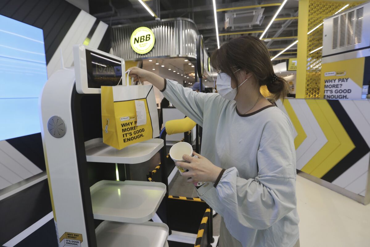 In this Sunday, Sept. 13, 2020, photo, a customer picks up a takeaway bag with food from a robot at No Brand Burger in Seoul, South Korea. These robotic services, with not a single face-to-face interaction, have been seen as a selling point amid the coronavirus pandemic and its restrictions. (AP Photo/Ahn Young-joon)