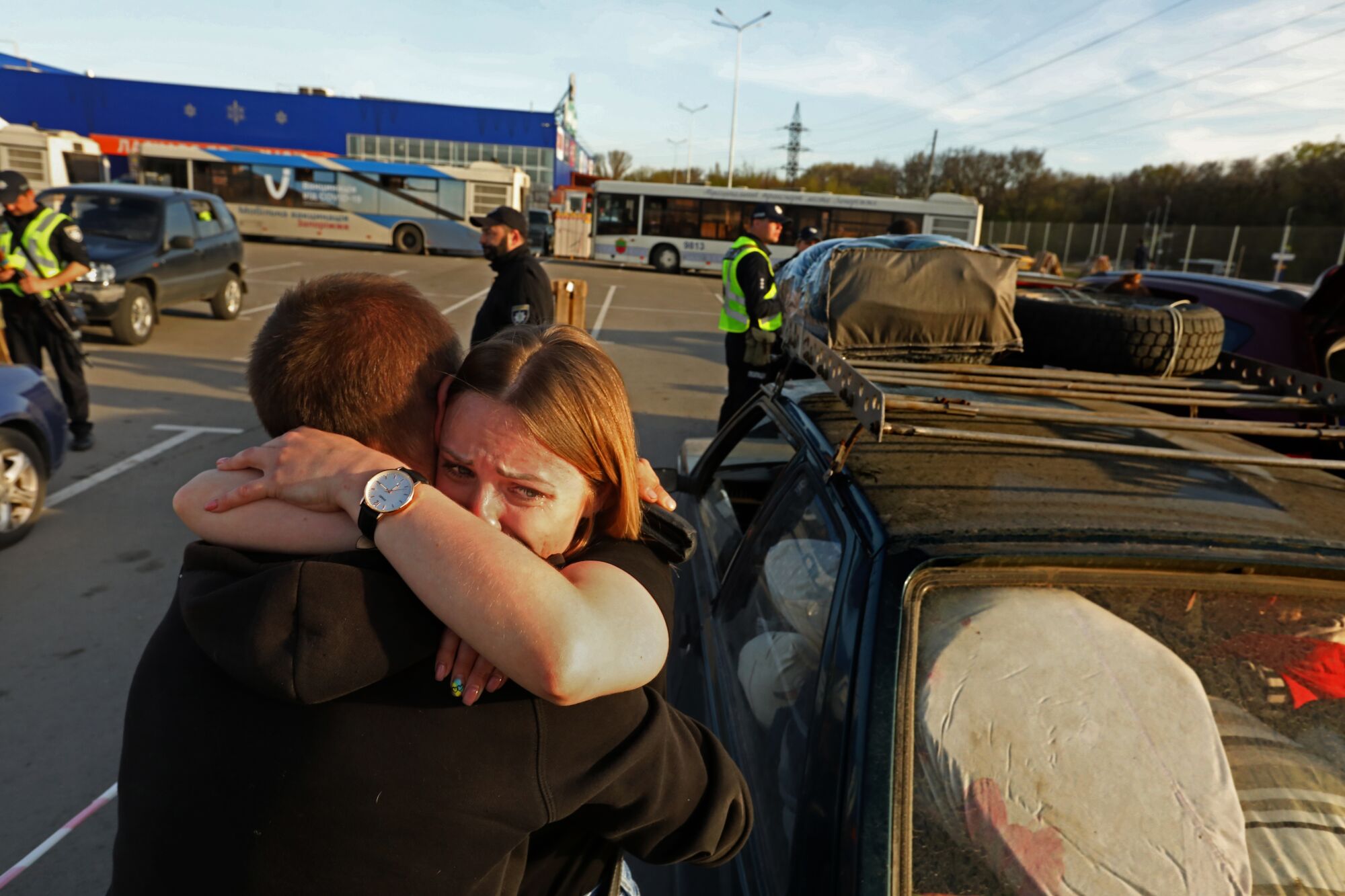 A woman throws her arms around her father in a parking lot full of buses and cars