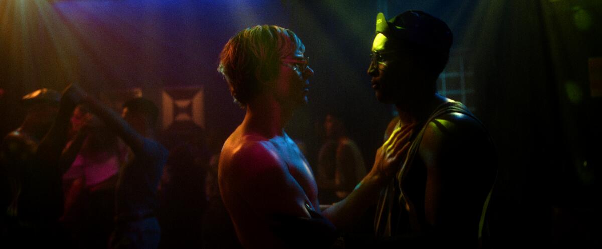 Evan Peters and Rodney Burford stand close in the colored lights of a dance club in "Monster: The Jeffrey Dahmer Story" 
