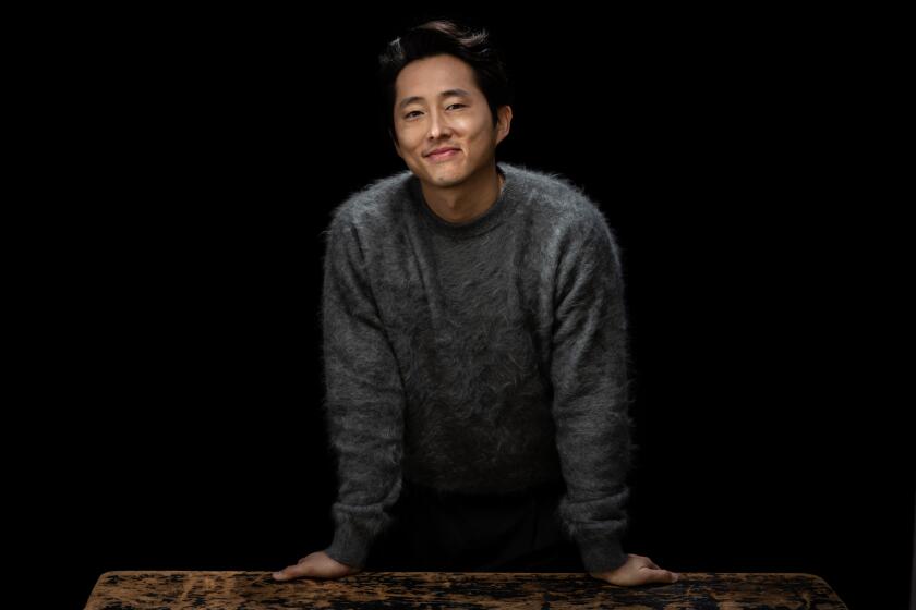 Steven Yeun posing in a gray sweater