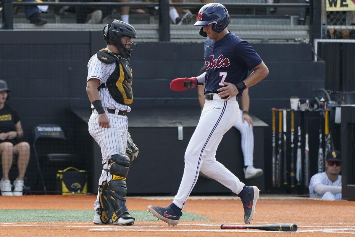 Southern Mississippi catcher Rodrigo Montenegro stands near the plate as Mississippi's Jacob Gonzalez scores during the third inning of an NCAA college baseball tournament super regional game Saturday, June 11, 2022, in Hattiesburg, Miss. (AP Photo/Rogelio V. Solis)