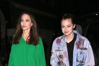 Angelina Jolie walks in a long green gown next to her daughter Shiloh who hears a patchwork shirt