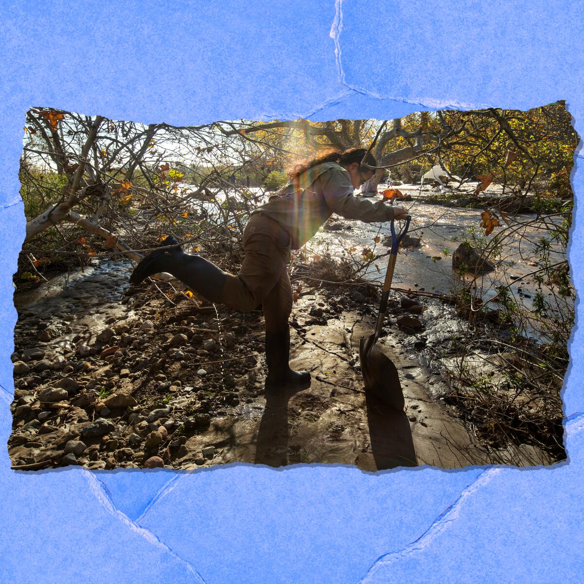 A person in mud boots leans over a shovel next to a running stream.