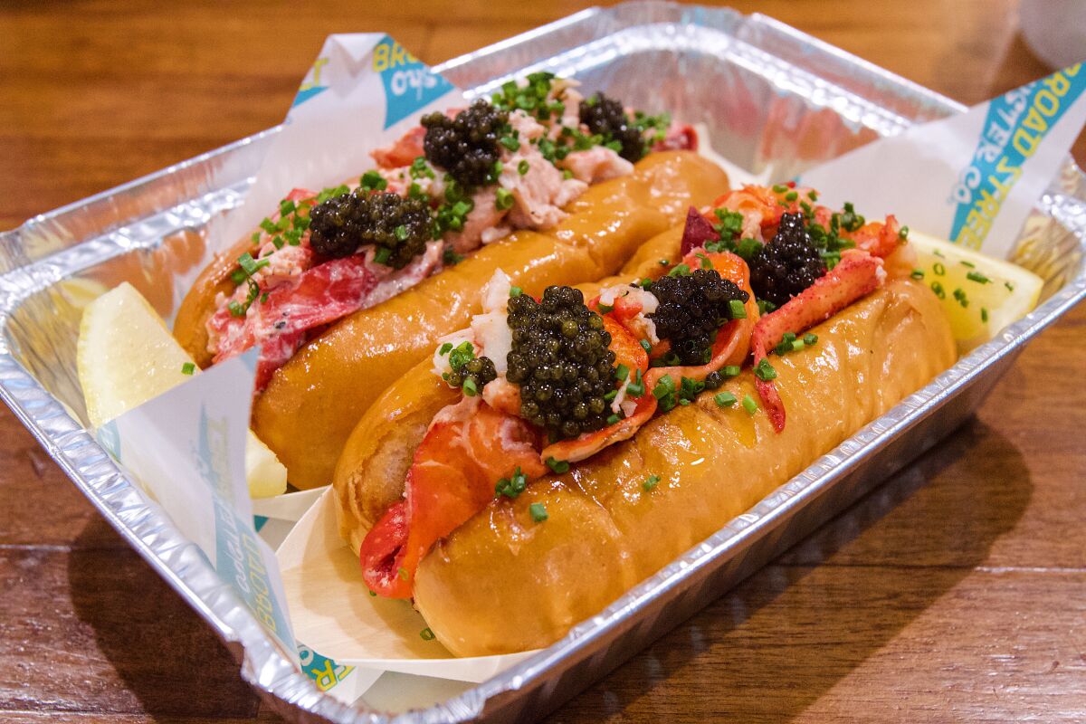 A buttered lobster roll and a chilled lobster roll, both in an aluminum to-go tin and topped with three dollops of caviar