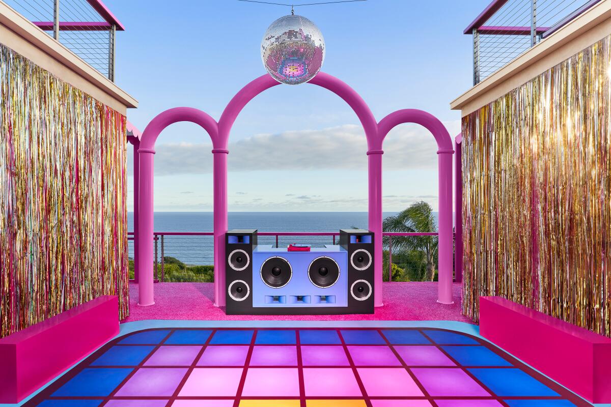 A view of the sea is framed by a checkered floor in bright colors, gold tinsel curtains and pink arches and a disco ball