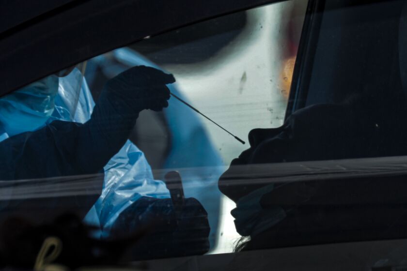 VICTORVILLE, CA - APRIL 02, 2020 - San Bernardino County health care worker takes a sample at a coronavirus COVID-19 drive-thru sample collection that took place at the county fairgrounds on Thursday April 02, 2020, Victorville. ( please keep the image dark / silhouetted to protect the privacy of the patient) (Irfan Khan / Los Angeles Times)