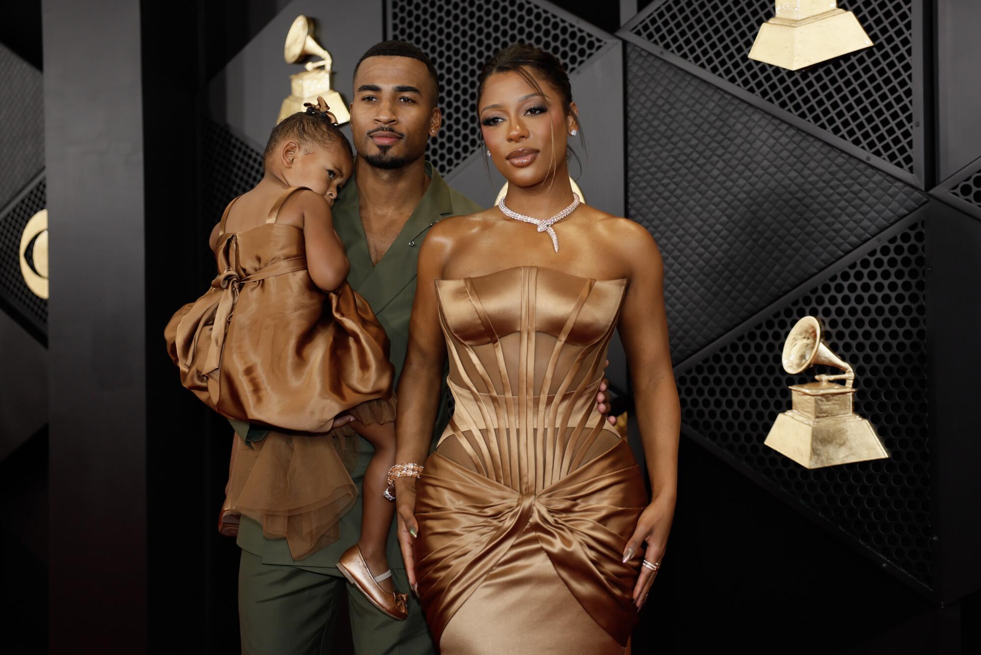 Victoria Monét in a bronze dress on the red carpet with John Gaines carrying their little girl Hazel