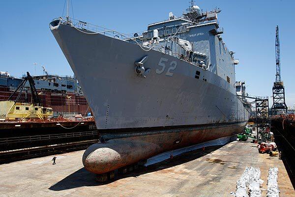 The amphibious warship Pearl Harbor in dry dock dwarfs a worker at the Nassco shipyard in San Diego, which took on a $20-million contract for repairs on the ship.